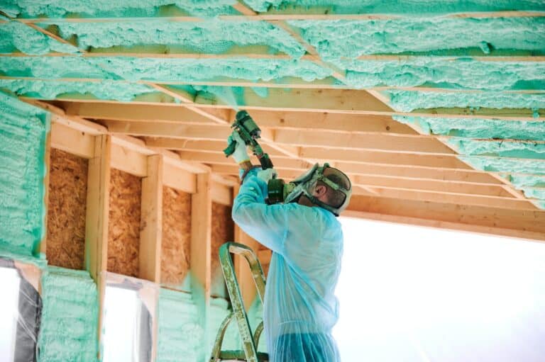 Worker spraying polyurethane foam for insulating wooden frame house.